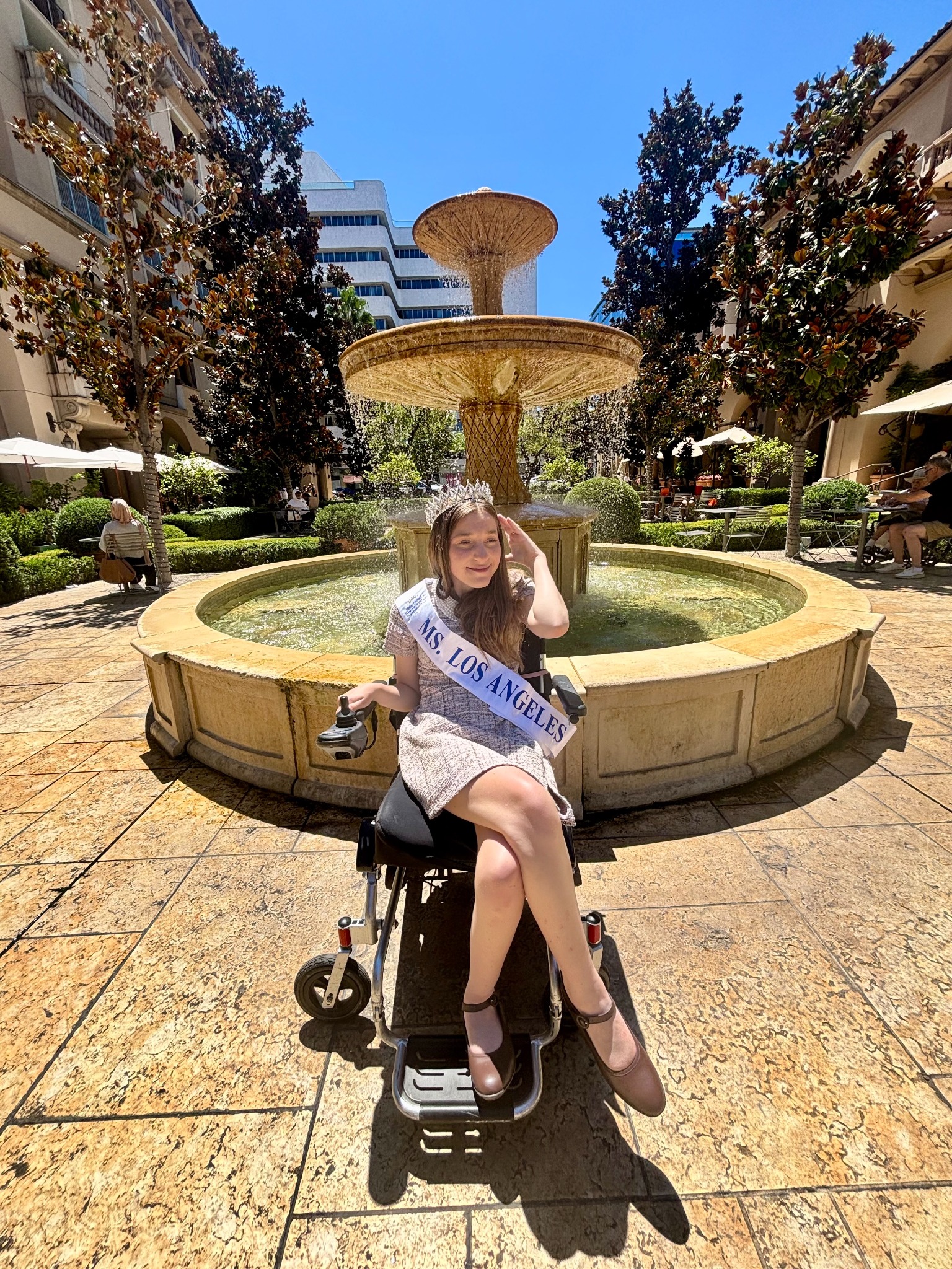Lilly Grossman wearing her Ms. Los Angeles crown and sash while seated in her power wheelchair.