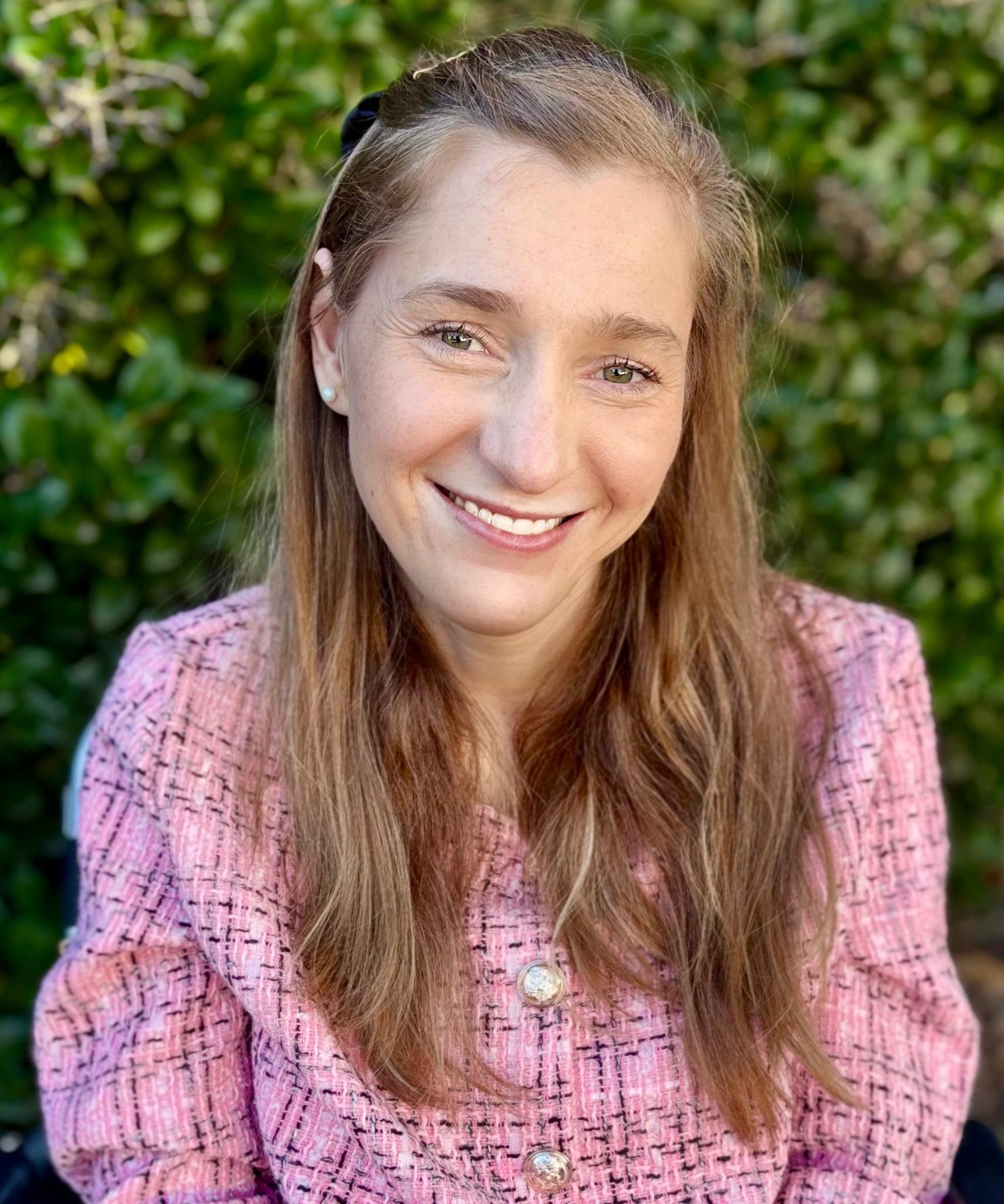 Lilly Grossman smiling outdoors in a pink tweed jacket.